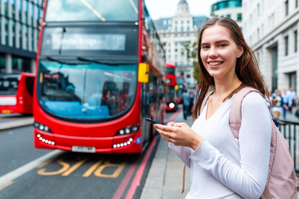 smiling-woman-with-smartphone-at-bus-stop-in-london